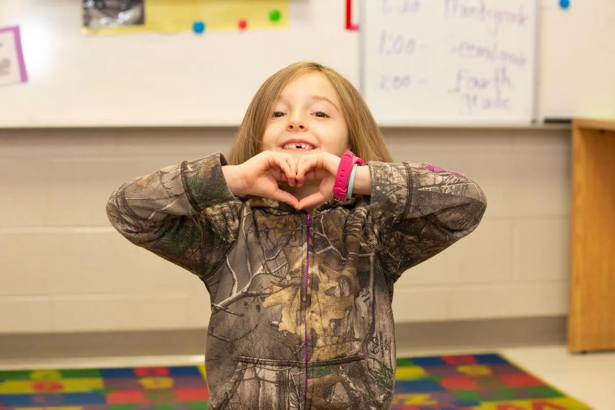 Smiling child making a heart shape with their hands in a classroom