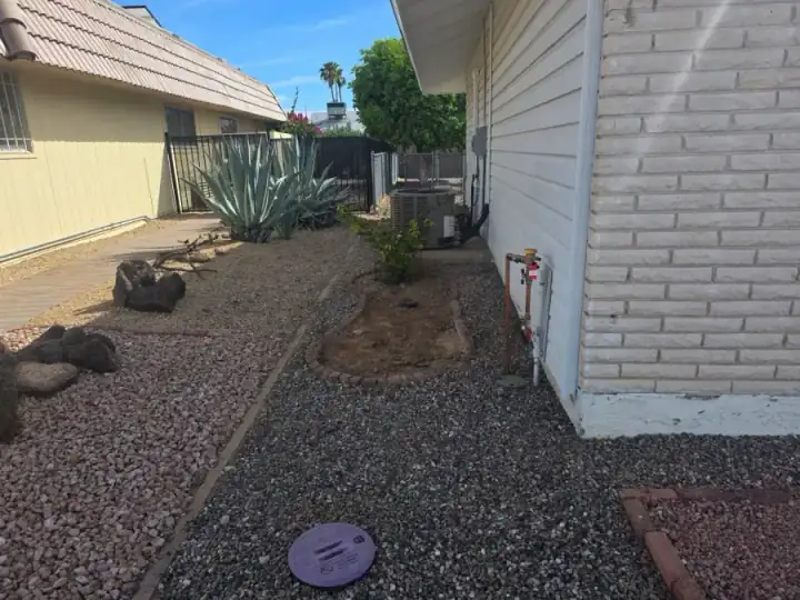 Established gravel landscape with an irrigation valve box, agave plants, and exterior equipment beside a home