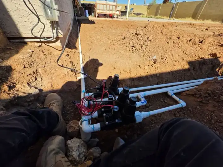 Irrigation valve assembly with white PVC piping in an open dirt trench