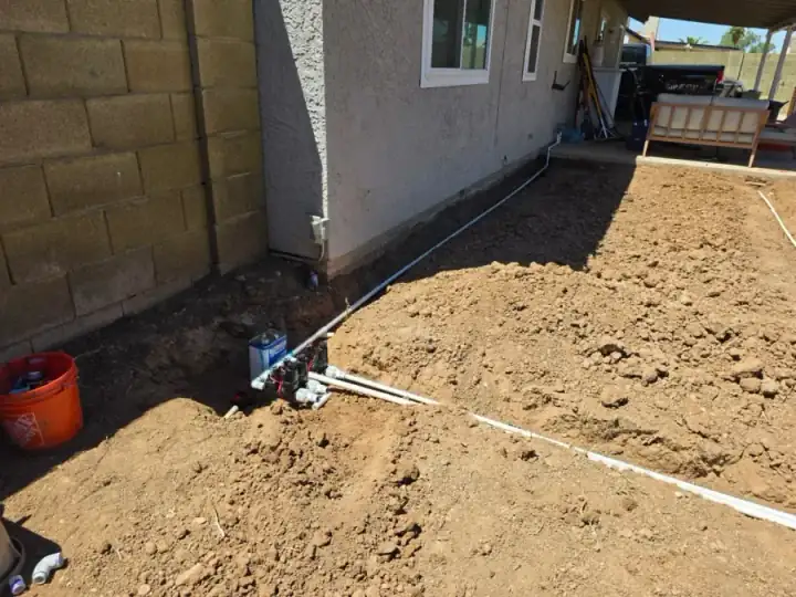 White irrigation pipe running through a prepared trench beside a house