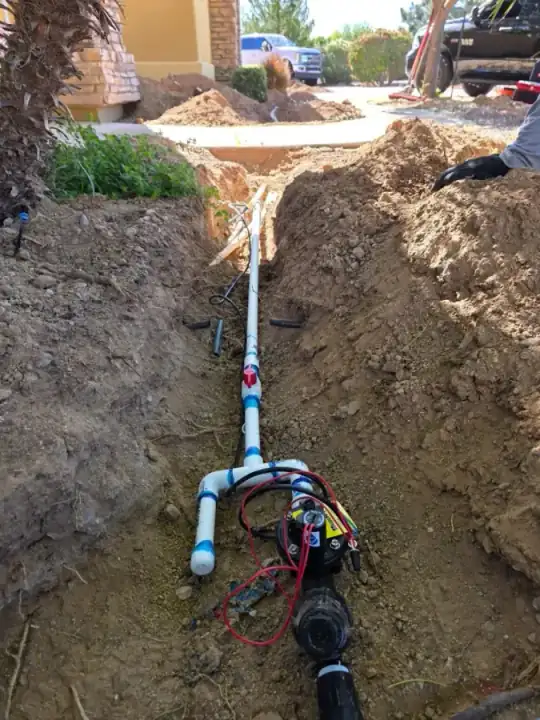 Long irrigation trench with white pipe and a valve assembly near a driveway