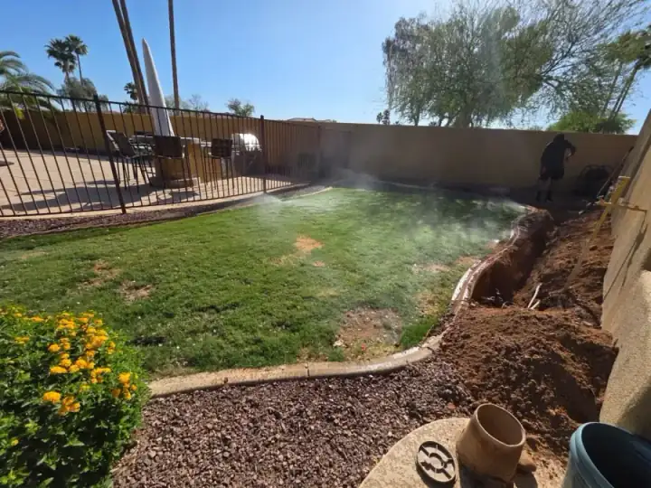 Sprinklers watering a lawn beside an open irrigation trench