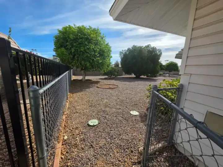 Residential gravel landscape with two green irrigation valve boxes and established trees